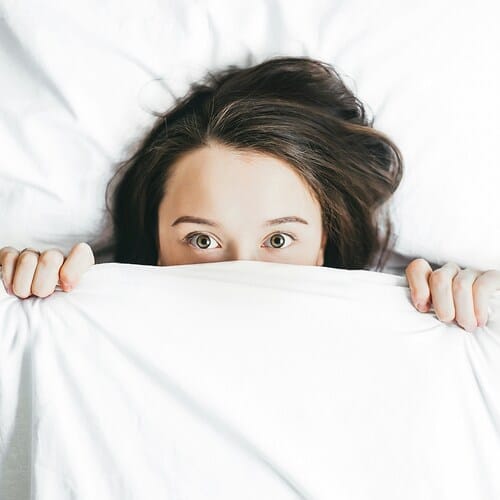 Frau, die sich aus Angst unter der Bettdecke versteckt.